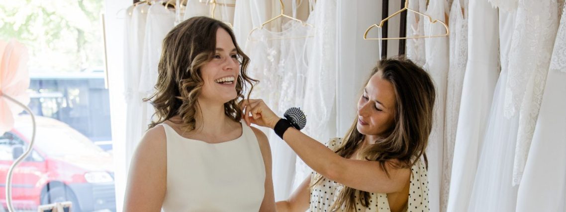 Brautkleid wird gerade von der Braut Stylistin in der Classique Brautboutique in Kiel abgesteckt. Braut strahlt mit einem lachendem Gesicht.