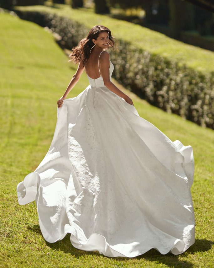 Braut läuft in einem Brautkleid mit langer Schleppe über den Rasen.