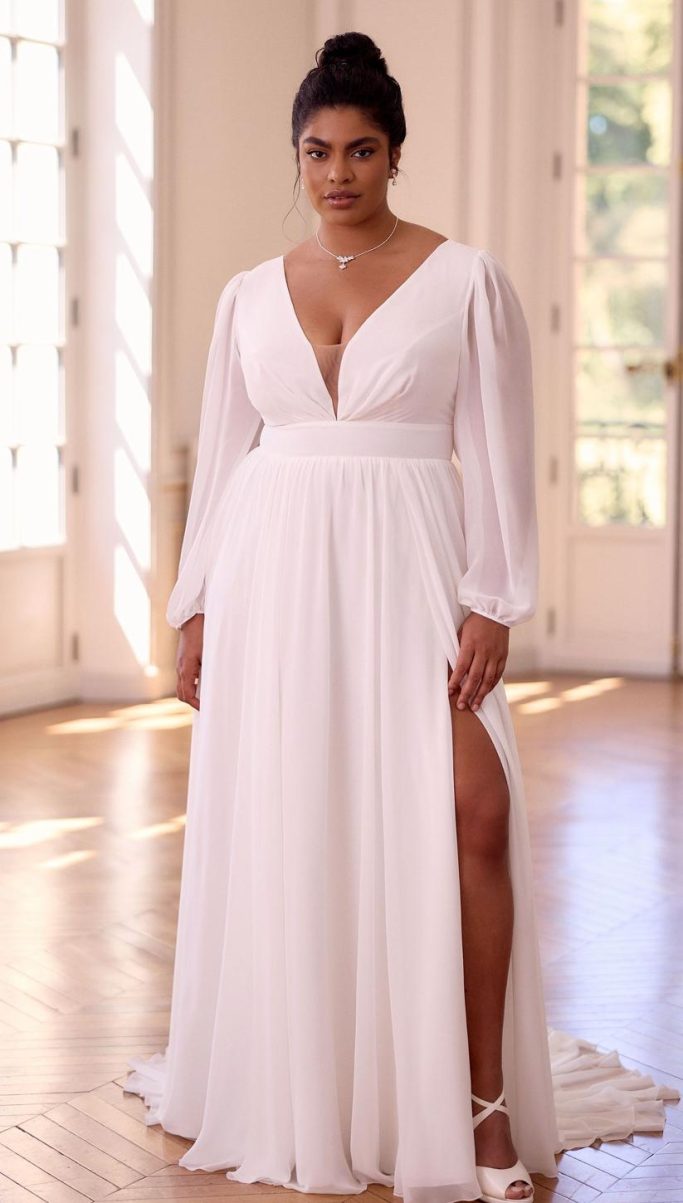 Plus Size Model in einem Schloss zeigt ein Brautkleid aus Chiffon mit langen Ärmeln und einem Beinschlitz.