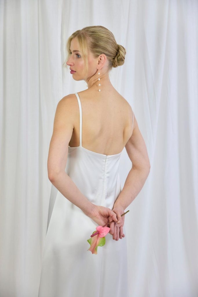 Braut steht mit einem Satin Kleid mit einer Blume in der Hand.
