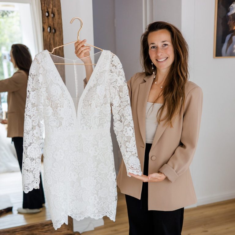 Ein kurzes Brautkleid mit besonderer Spitze wird von der Inhaberin der Classique Brautboutique in Kiel am Bügel präsentiert.