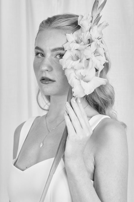 Model hält Blume neben dem Kopf für ein romantisches Detailbild.
