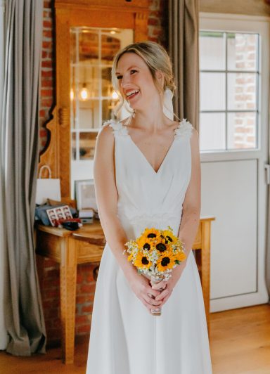 Braut von vorne fotografiert strahtl mit Brautstrauß aus Sonnenblumen.
