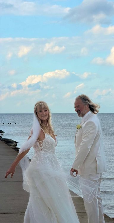 Braut und Bräutigam stehen auf einem Steg am Meer und der Schleier weht im Wind