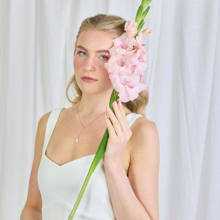 Braut am Ostseestrand bei einer Strandhochzeit. Ein Oberteil mit pastellfarbigen Blumen und einen Brautstrauß in der Hand.