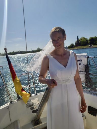 Braut auf einem Segelboot am Segeln im Brautkleid.