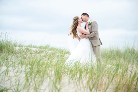 Braut und Bräutigam stehen in den Dünen am Strand und küssen sich