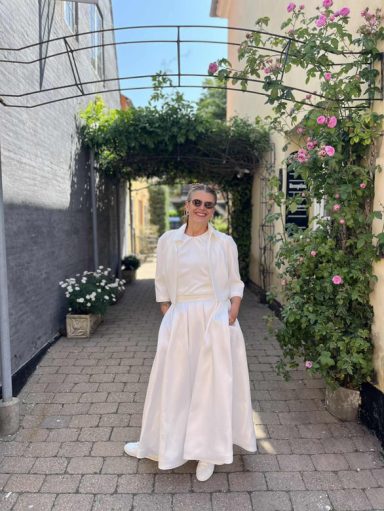 Braut im Zweiteiler mit Blumen im Hintergund.