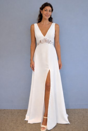 LAMBERT CREATIONS Braut schaut lächelnd mit einem weißen Brautkleid mit Beinschlitz in die Kamera.